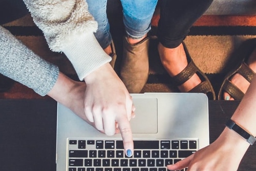 Three pairs of hands pointing to laptop