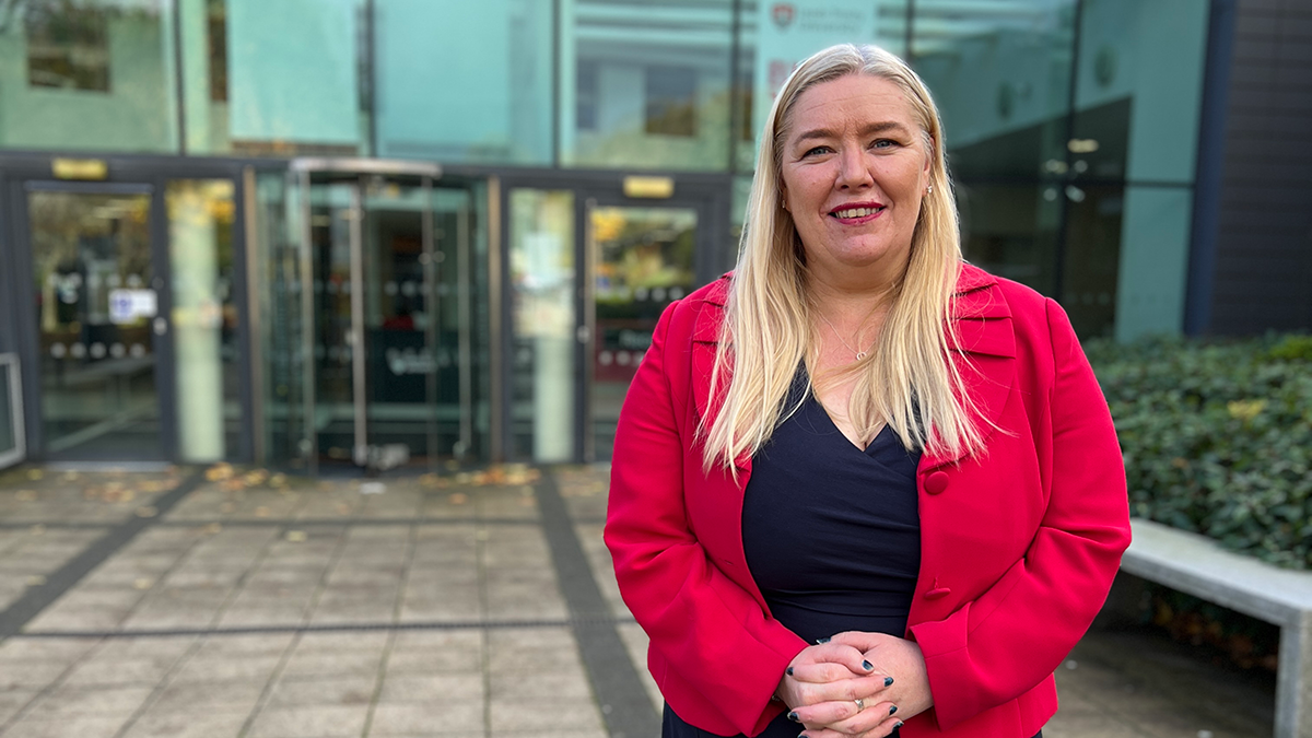 A female academic with long blonde hair and wearing a red jacket smiling.