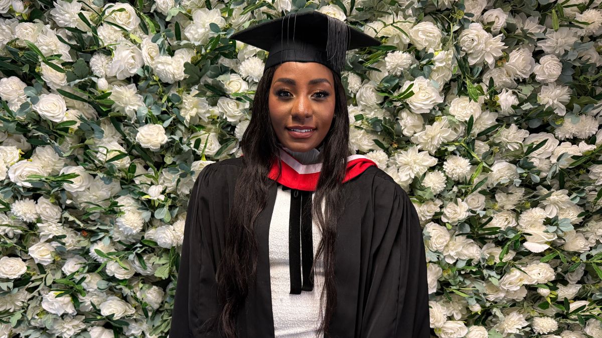 A female graduate poses for a picture in front of a white flower wall