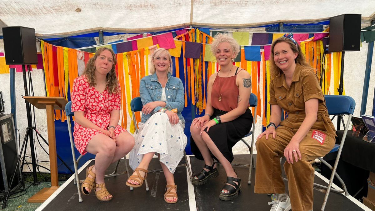 Four women smile while sitting on a stage in front of a colourful background.