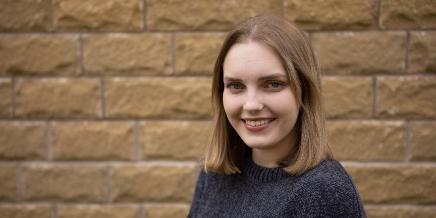 Brunette female in charcoal jumper in front of brick wall