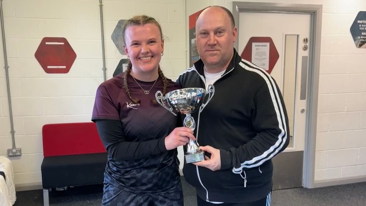 A female student a male member of staff smile while holding a trophy