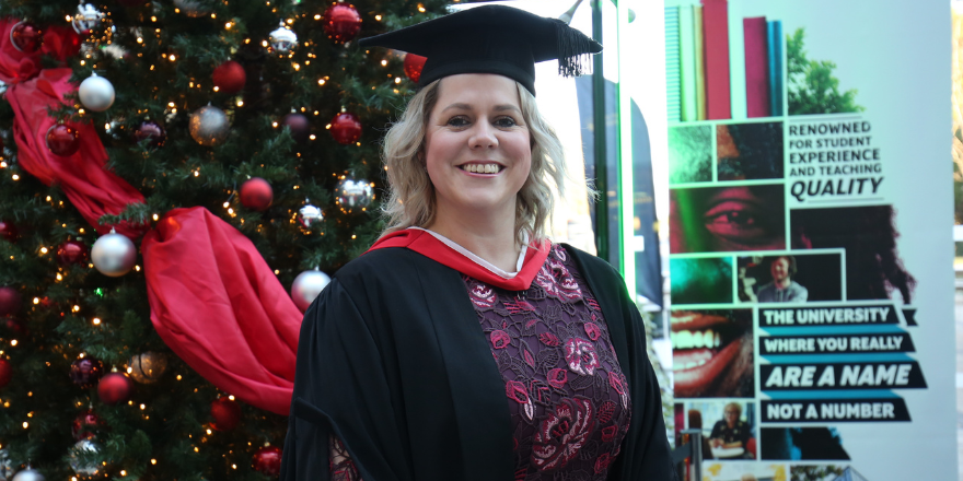 Blonde female in graduation cap stands in front of Christmas tree