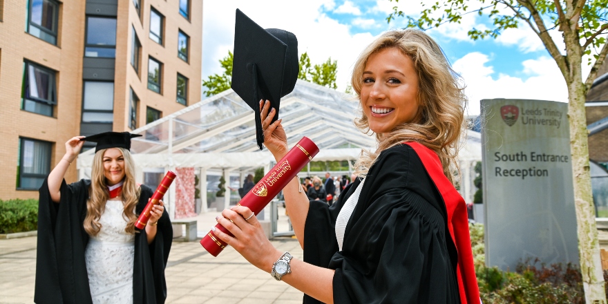 Students wearing gowns and holding certificate tubes on Leeds Trinity campus