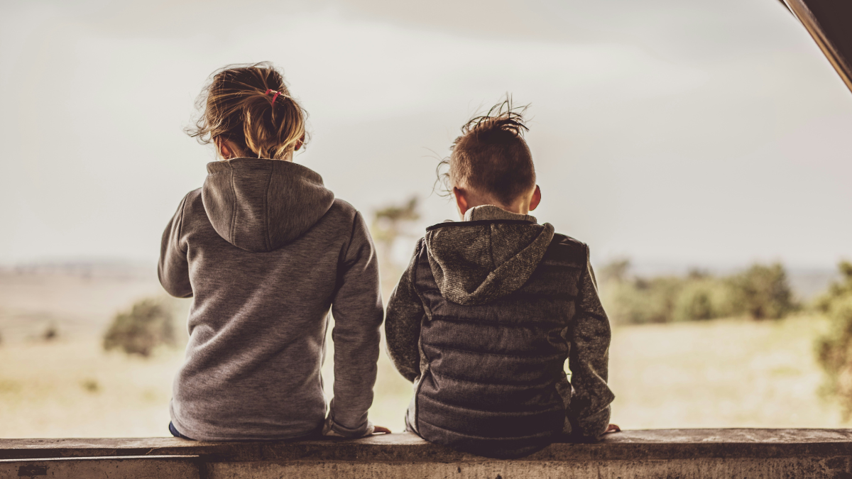 Two children in dark grey clothing with their backs turned.