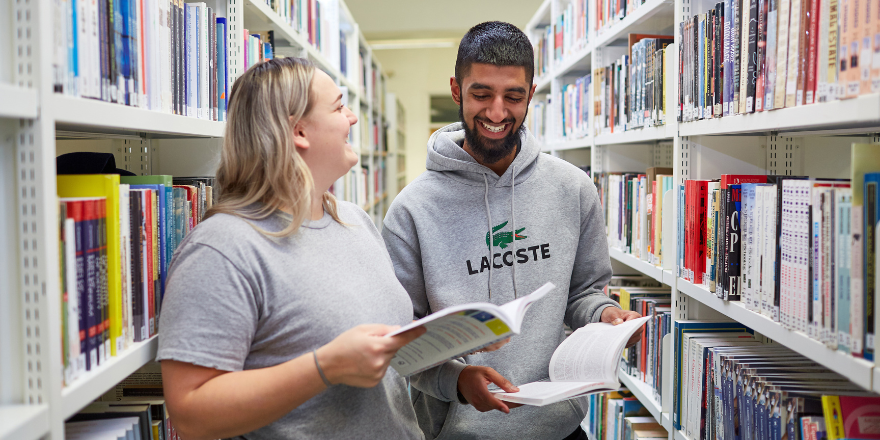 Two students in the library, holding books.