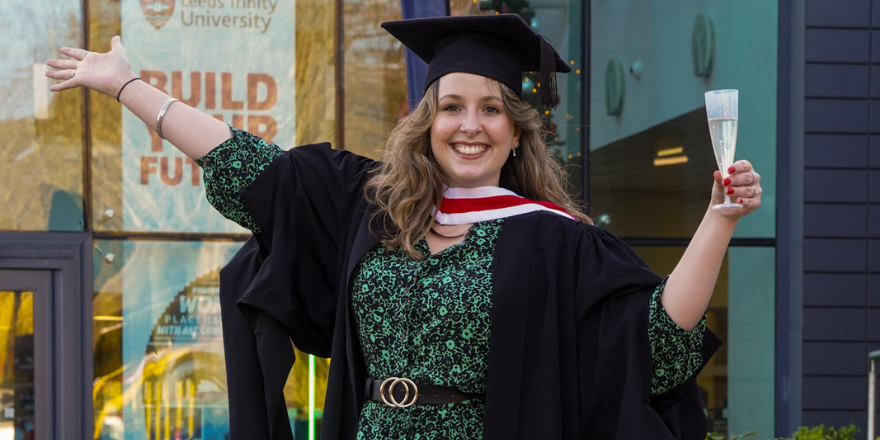Smiling female graduate in cap and gown poses with arms outstretched