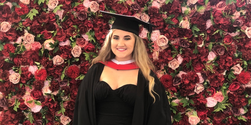 Female student in cap gown and black dress with red floral background