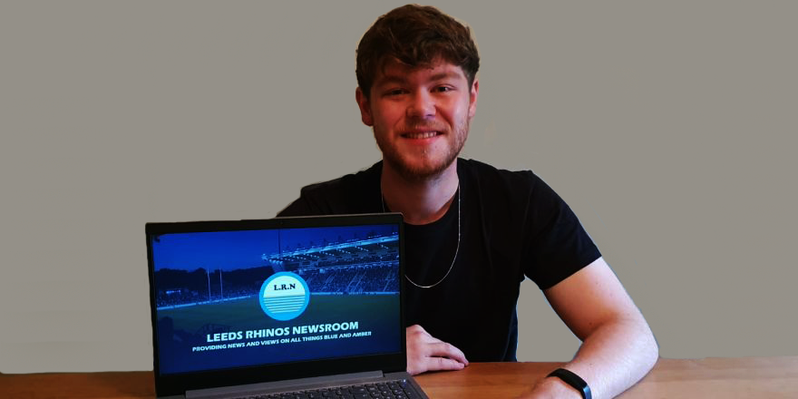 Male with black t-shirt and brown hair with laptop open on blue webpage