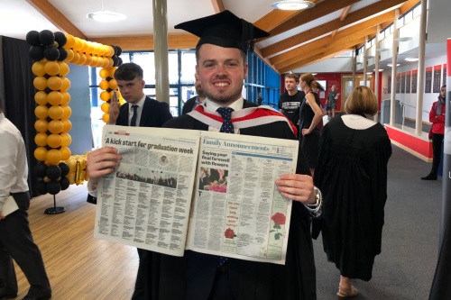 Tom pictured in cap and gown holding up newspaper