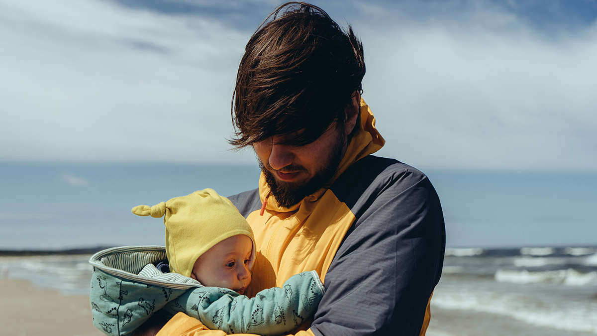A young dad holding his baby on the beach.