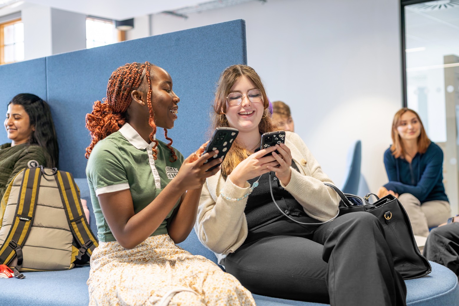 Students in Leeds City Campus Social Space laughing while looking at their phones..
